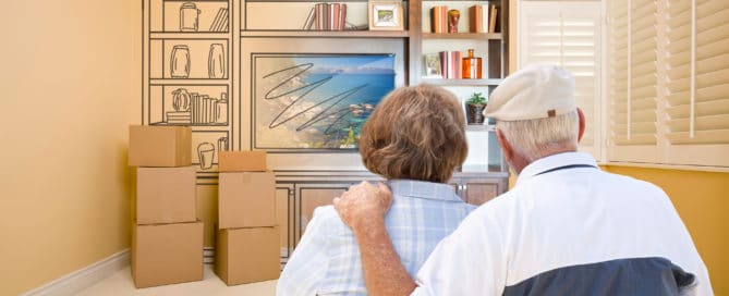 Senior Couple In Room With Moving Boxes Looking At Drawing of Entertainment Unit.