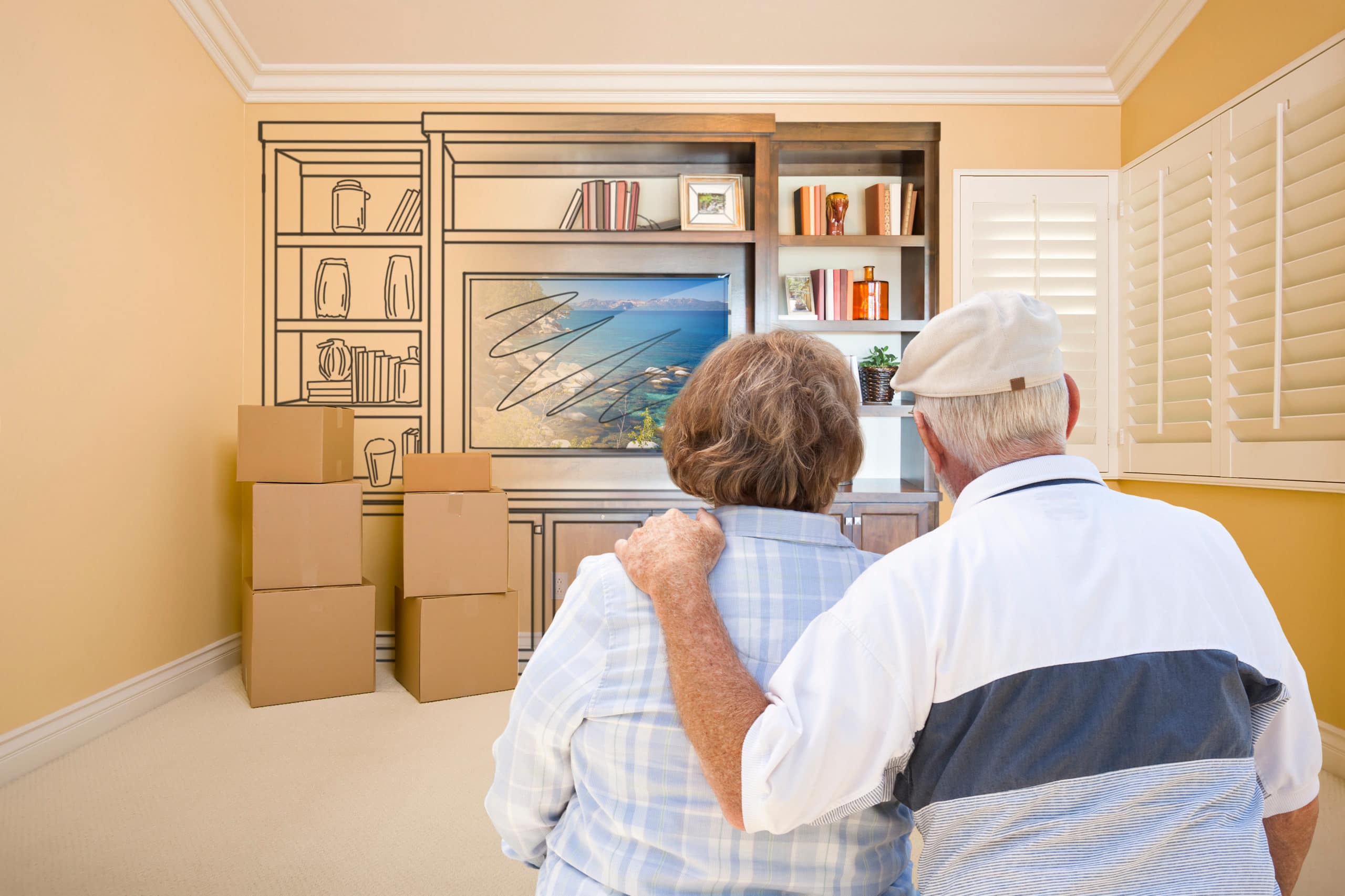 Senior Couple In Room With Moving Boxes Looking At Drawing of Entertainment Unit.